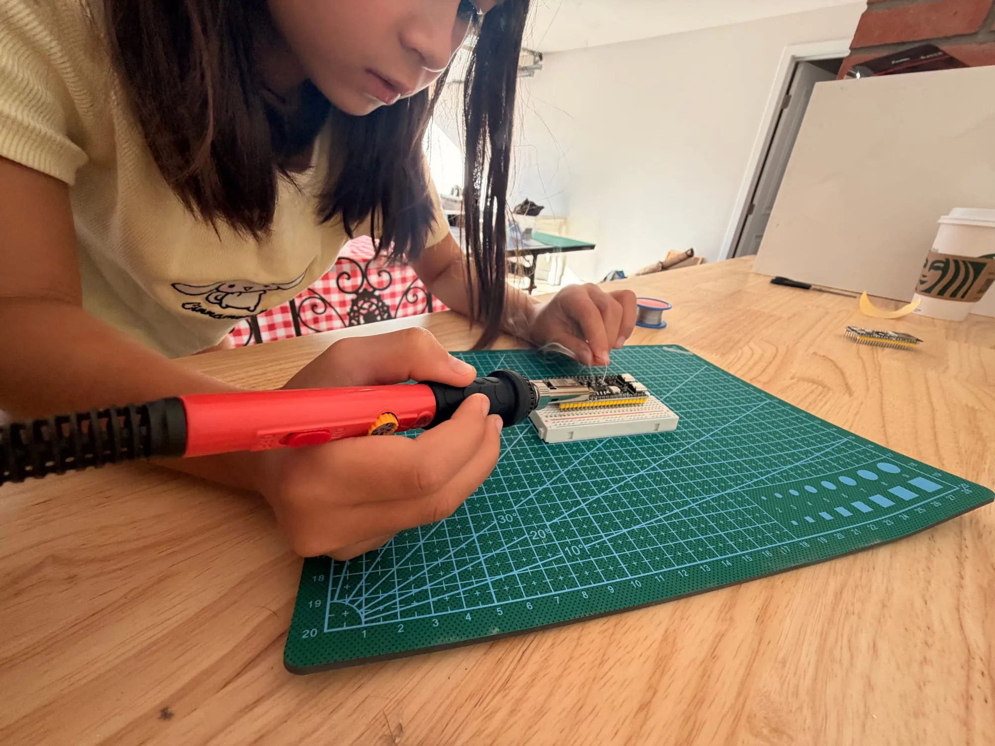 Evelyn leaning over a cutting mat, soldering header pins onto an ESP32 board seated in a breadboard